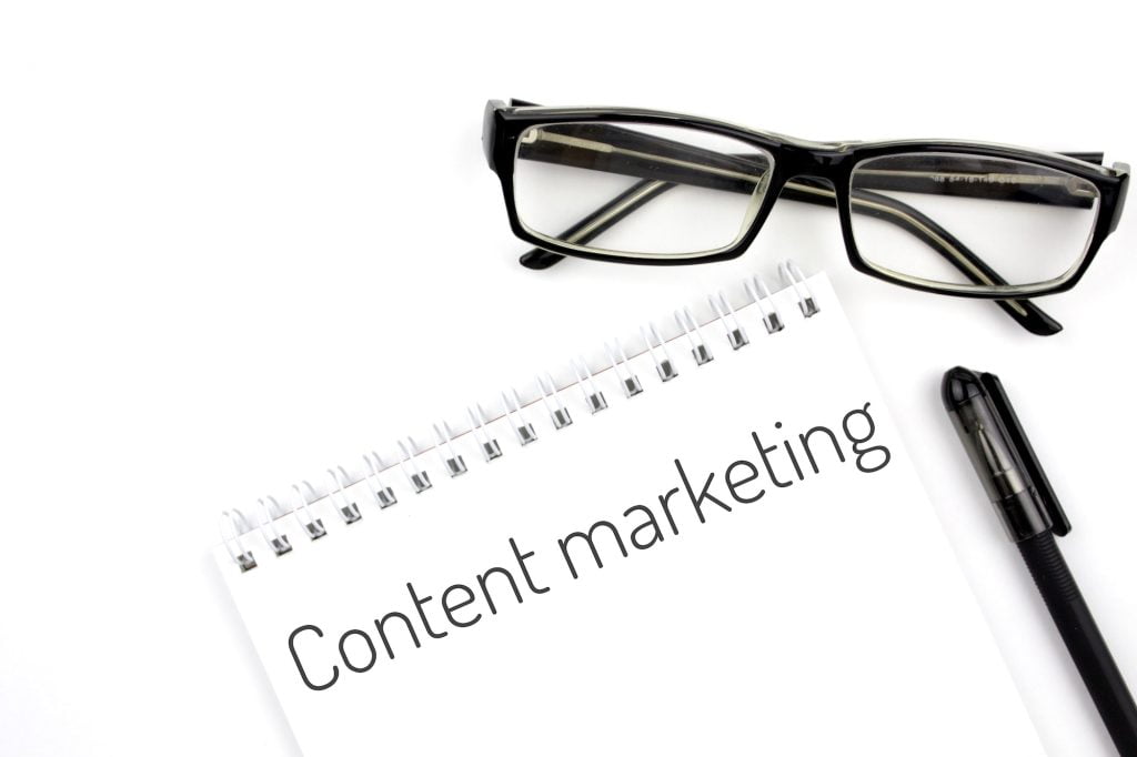 Reading glasses and notebook with word content marketing on a white background