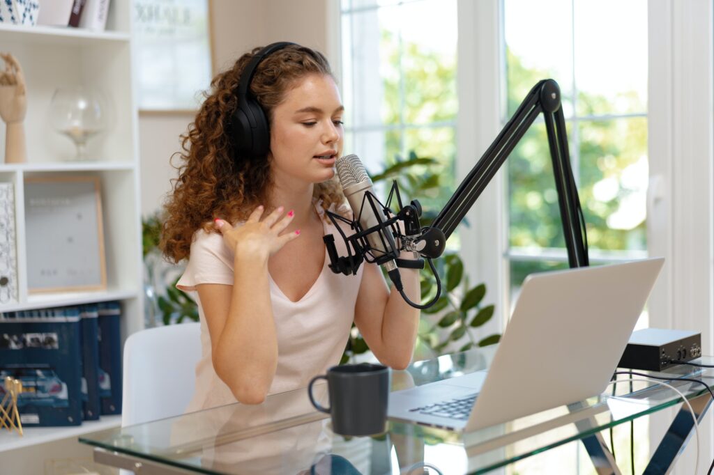 Young curly female recording podcast from home and talking into a microphone - content marketing strategies for small businesses.